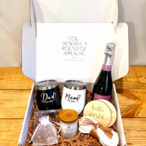 A box with champagne, wine glasses, and a baby announcement.