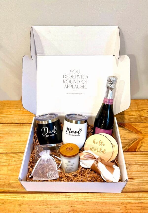 A box with champagne, wine glasses, and a baby announcement.
